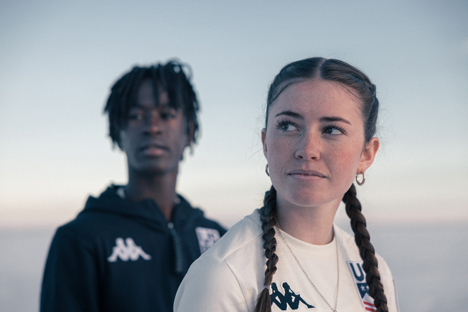 Close up from the chest up of Male and female US athlete looking off into the distance wearing Kappa collection 